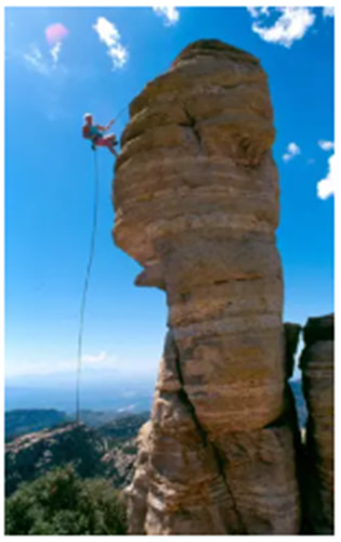 a guy climbing up the side of a tall rock formation in the mountains