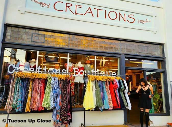 a woman is looking over a rack of dresses outside a boutique