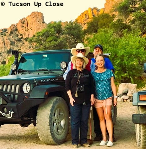 four adults standing beside a jeep in a desert setting with rocky cliffs in the background