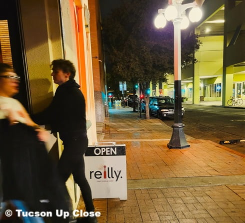 entry sign to a restaurant with people going in and out on an evening