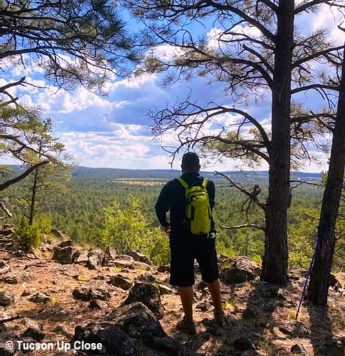 Man with backpack looking from a mountain top into a valley below.