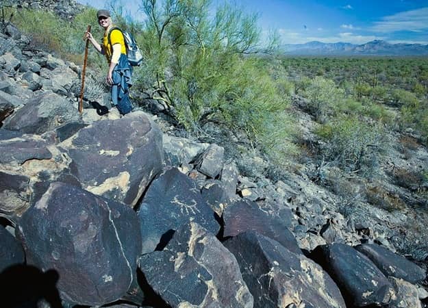 man with walking stick hiking up a hill with boulders etched with petroglyphs