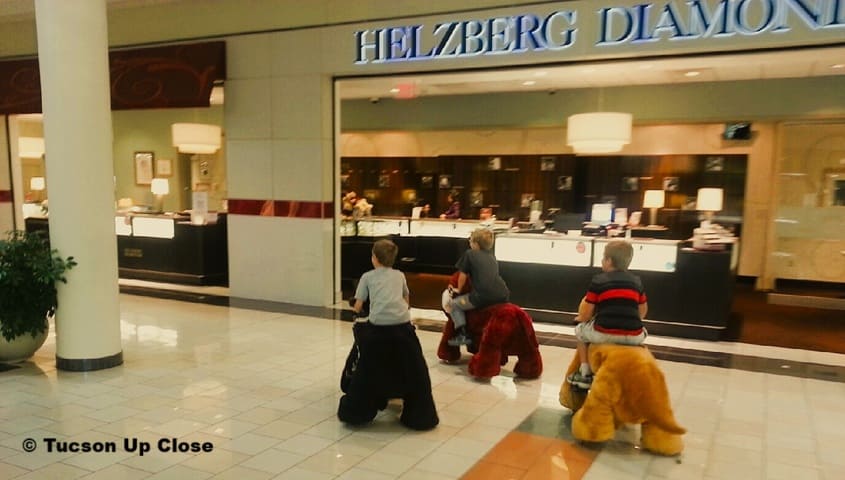 three boys riding on stuffed animals in a mall
