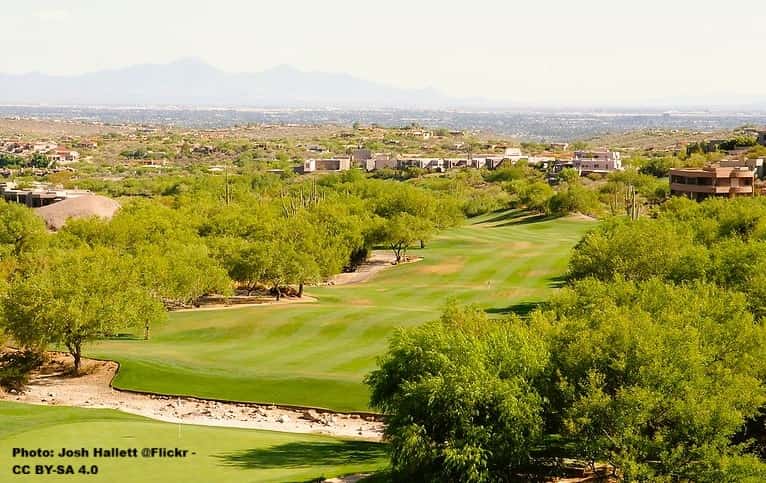 Grassy gold course amidst trees overlooking a cityscape.