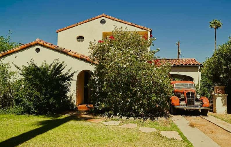 two story home with tile roof and antique vehicle in the driveway